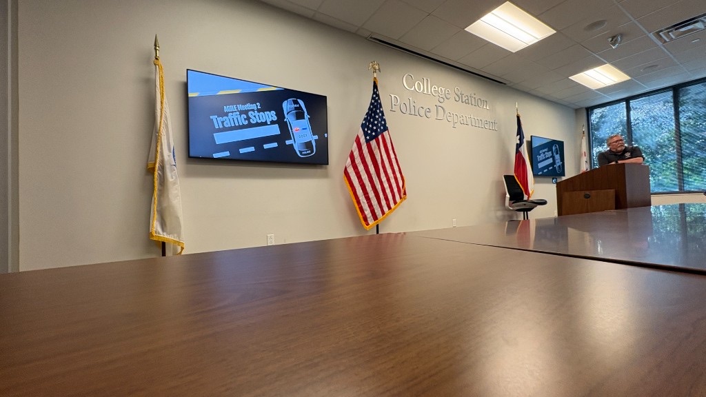 An officer at a podium during AGILE's spring tour at College Station Police Department, with the U.S. and Texas flags behind him.